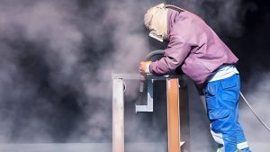 Technician in full safety gear performing abrasive blasting inside a blast room, representing a professional solution for those searching “sandblasting near me.”