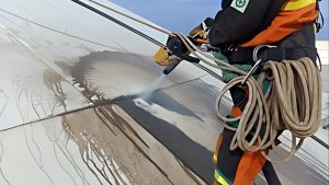 Technician in safety gear using pressurized equipment to clean a large surface, visually demonstrating the sandblasting definition through the removal of dirt and coatings with a high-pressure liquid abrasive.