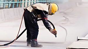 Worker in protective gear applying a sandblasted concrete finish to a large flat surface using a sandblasting hose on a construction site.