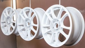 Powder-coated rims hanging for finishing at a sandblasting service. Search for sandblasting rims near me to restore and enhance your wheels.