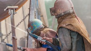 Workers in protective gear using sandblasting equipment, showing the process related to can you sandblast wood.
