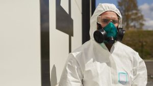 Person wearing a protective hazmat suit and respirator mask for safety during hazardous material handling.