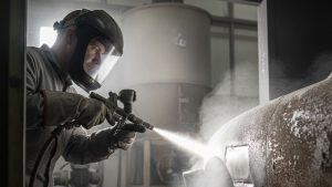 A professional sandblaster using equipment to clean a metal surface, demonstrating the how much does sandblasting cost for metal surface preparation.