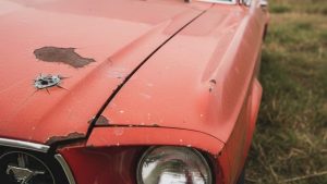 Close-up of a car hood with peeling and chipped paint, showcasing the wear and tear of the vehicle's exterior.