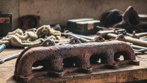 A rusty automotive part on a workbench surrounded by tools, illustrating the need for car sandblasting near me to remove rust and restore vehicle surfaces.