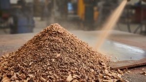 Pile of walnut shell sandblasting media on a work surface with abrasive blasting in progress, showing natural media used for controlled surface cleaning.