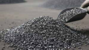 Steel grit blasting media being poured into a pile, showing angular steel grit particles used for abrasive blasting and surface preparation.