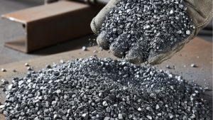 Steel grit blasting media held in a gloved hand above a pile of angular steel grit, illustrating abrasive blasting media used for industrial surface preparation.