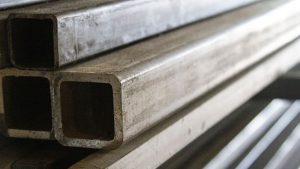 Stacked rectangular stainless steel tubing with visible surface wear and light oxidation, showing industrial metal material used for fabrication and construction