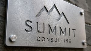 Sandblasted steel finish business sign for Summit Consulting mounted on a wall with brushed metal texture and engraved logo lettering.